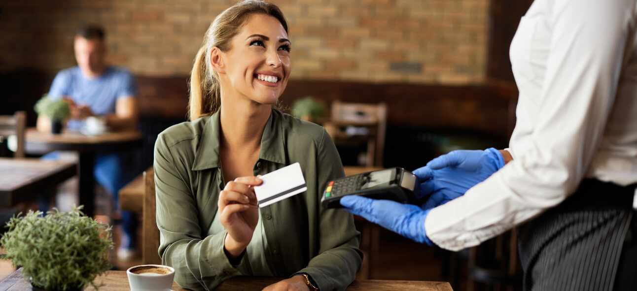 A happy woman makes a card payment seated in a cafe